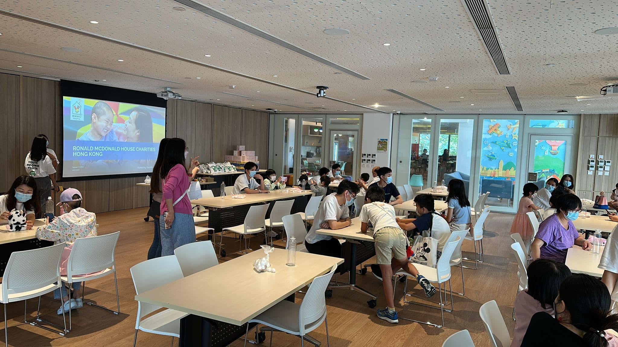 A wide view of the session room at RMHC Hong Kong, families at tables working on the craft activity, with a Ronald McDonald House Charities Hong Kong slide on the screen